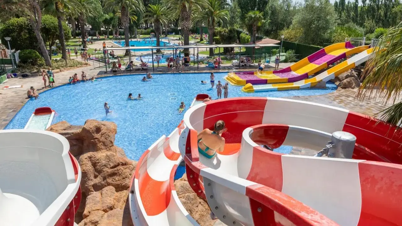 Disfruta de los mejores campings de Catalunya con piscinas y toboganes acuáticos. Familias se divierten en un día soleado.