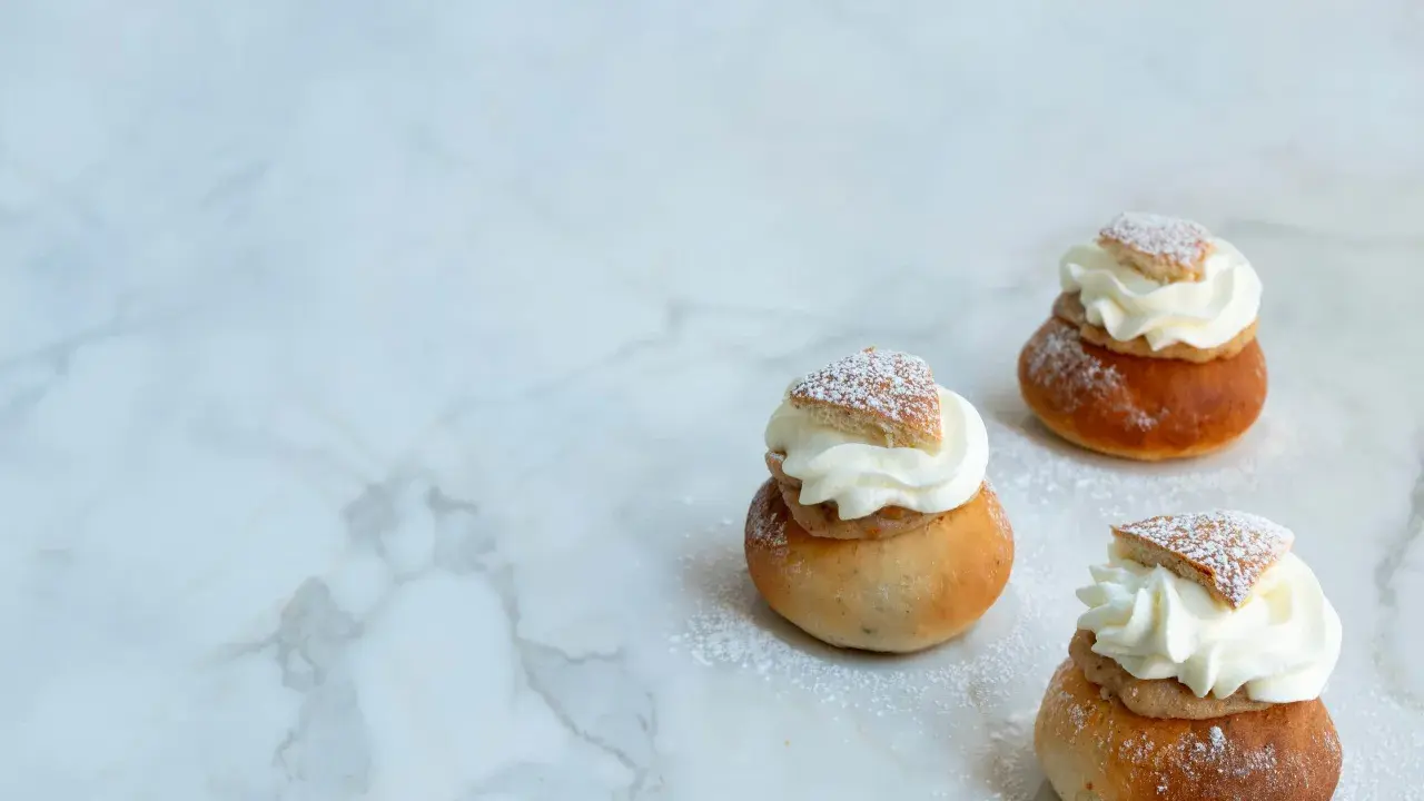 Tre semlor utan mandelmassa, toppade med vispgrädde och pudersocker, ligger på ett marmorbord.