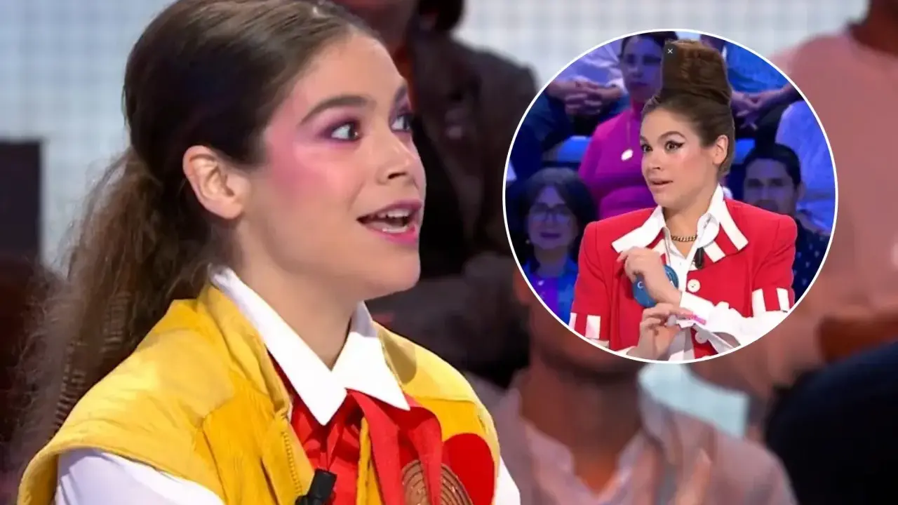 Cosima Ruiz de la Prada, con maquillaje llamativo y un chaleco amarillo, habla en un programa. En un círculo, se ve su peinado alto y chaqueta roja.