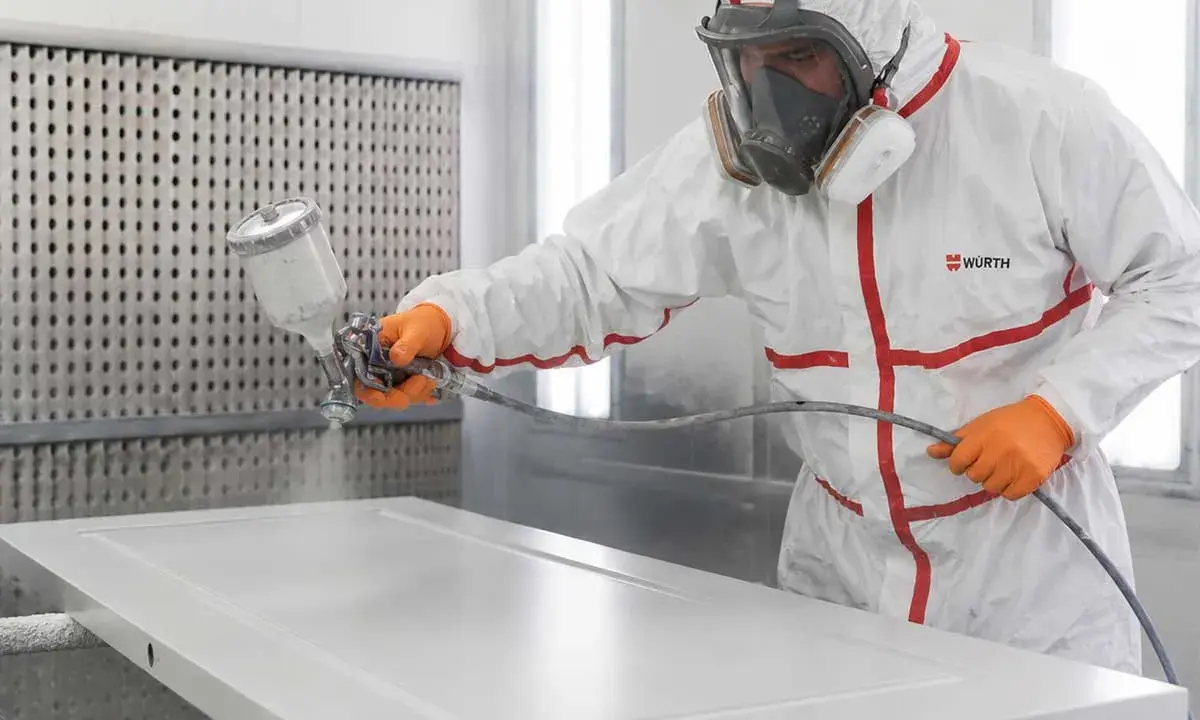 Profesional aplicando pintura blanca a una puerta con pistola pulverizadora. Aprende como lacar puertas en blanco para un acabado perfecto.