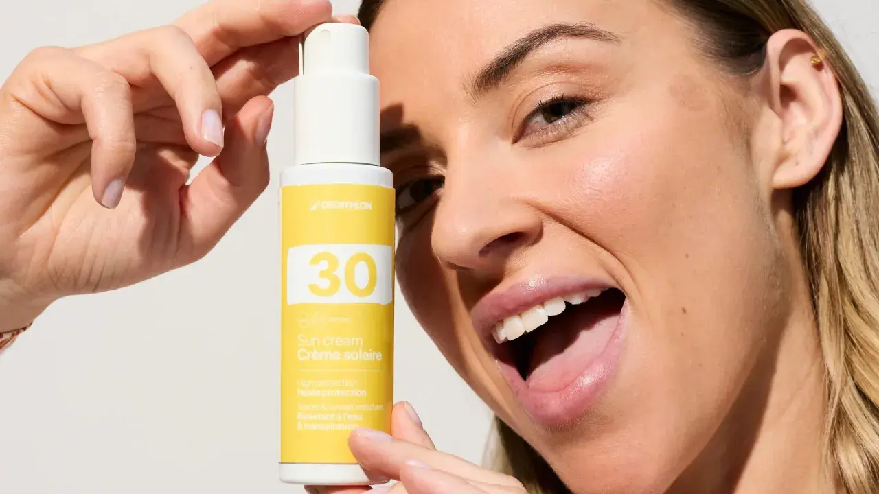 Une femme souriante tient un flacon de crème solaire visage SPF 30. La quantité de crème solaire est parfaite pour une protection optimale.