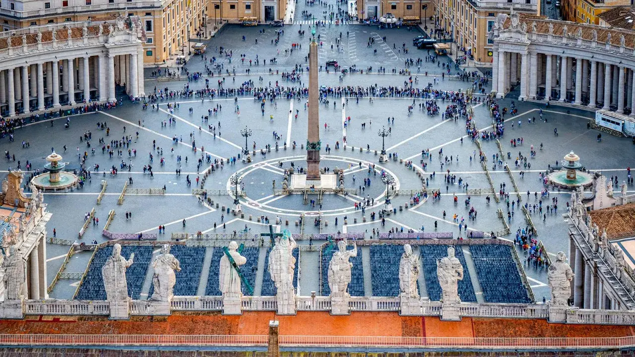 Vue aérienne de la **place du Vatican**, avec son obélisque central, ses fontaines et une foule de visiteurs.