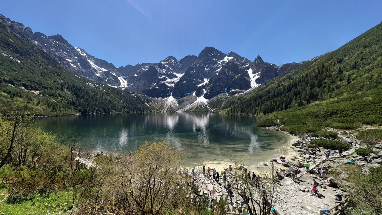 Widok na Morskie Oko z górami w tle i turystami na brzegu.