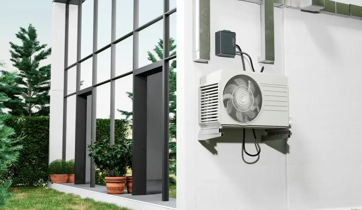 Unité extérieure d'une pompe à chaleur installée sur un mur blanc, à côté d'une maison moderne avec de grandes fenêtres. Comment choisir quelle pompe à chaleur choisir pour votre maison ?