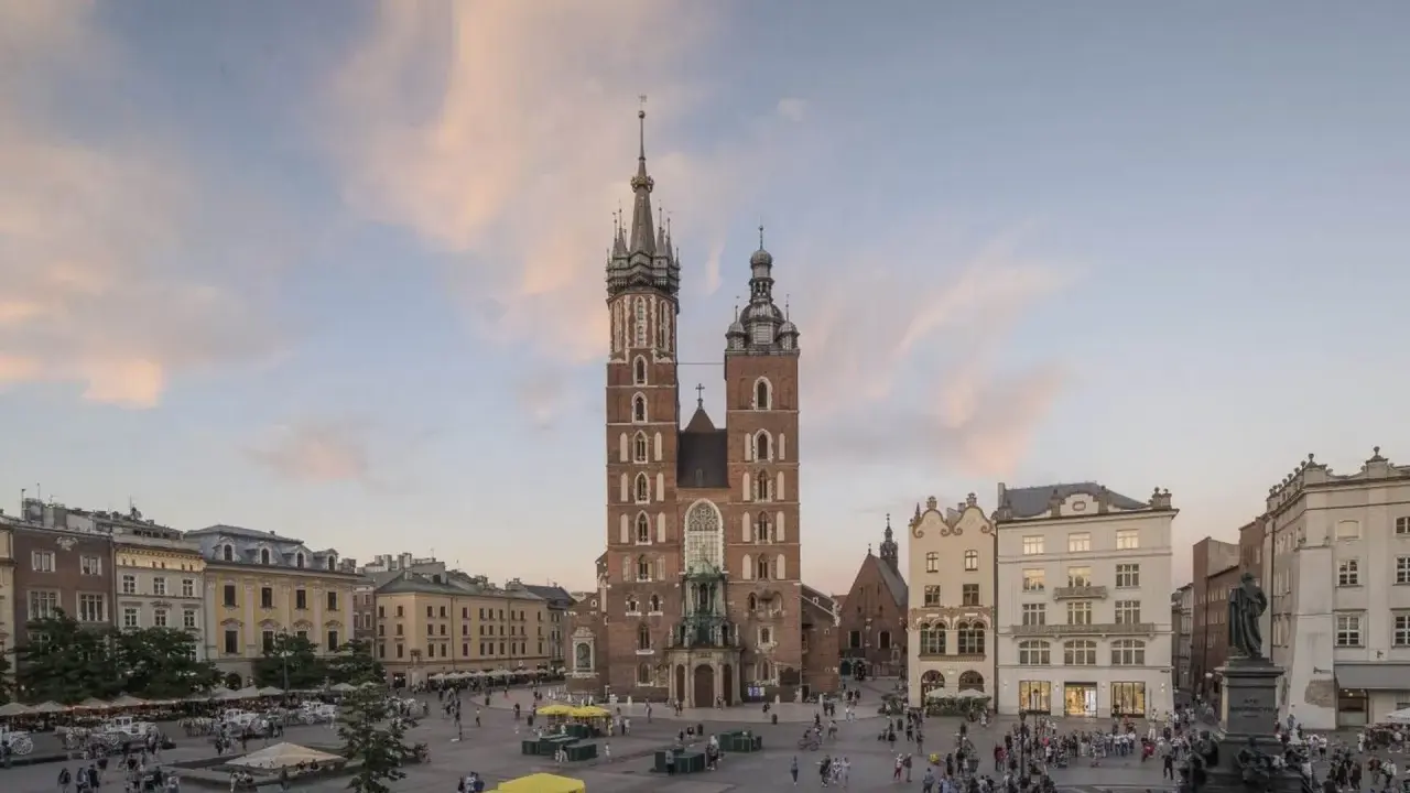 Majestatyczna Bazylika Mariacka góruje nad Rynkiem Głównym w Krakowie. Tłumy spacerują, podziwiając architekturę i atmosferę miasta.