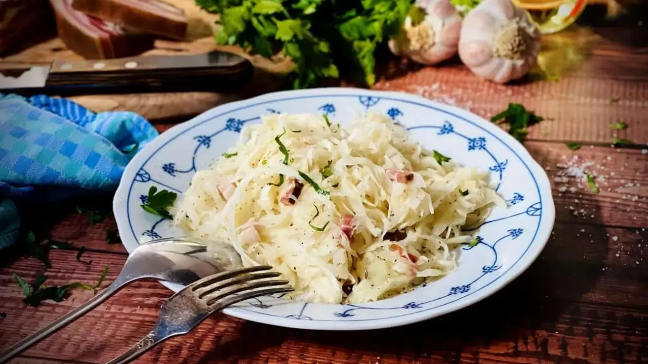 Ein Teller mit Krautsalat, garniert mit Petersilie. Daneben liegen Gabel und Löffel. Ein leckeres Krautsalat Rezept für dich!