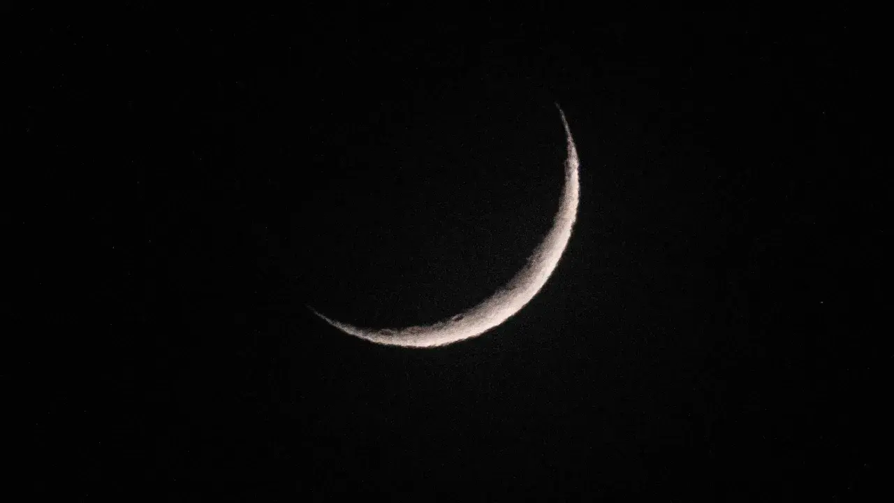 Eine schmale Mondsichel leuchtet im dunklen Nachthimmel. Sie erinnert an den Beginn von Ramadan, wann die Zeit des Fastens beginnt.
