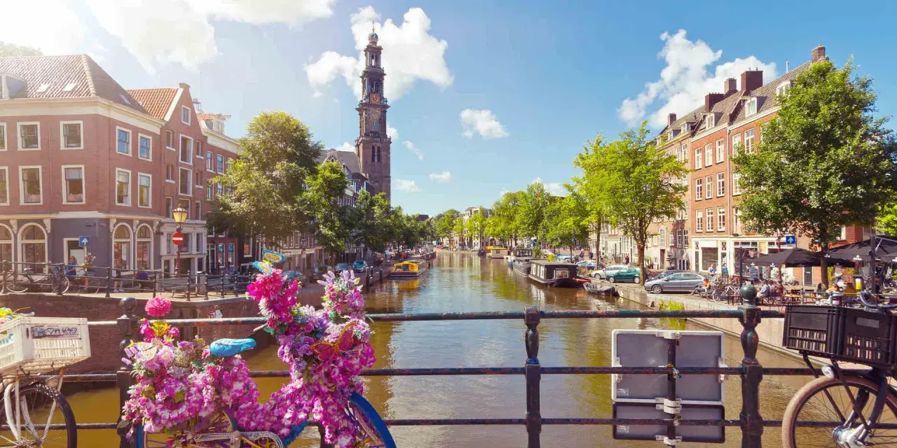 Das **beste von Amsterdam**: malerischer Kanal mit Booten, historischen Gebäuden und einem Kirchturm. Blumenverzierte Fahrräder auf einer Brücke.