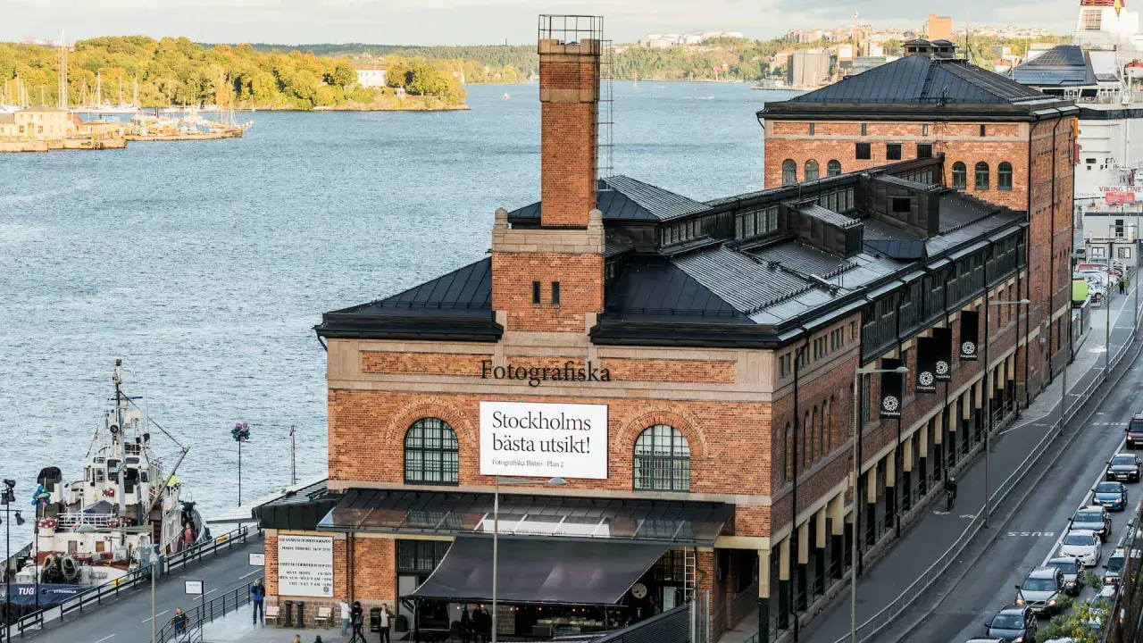 Fotografiska Stockholm vid vattnet, med en båt i förgrunden och en stadssilhuett i bakgrunden.