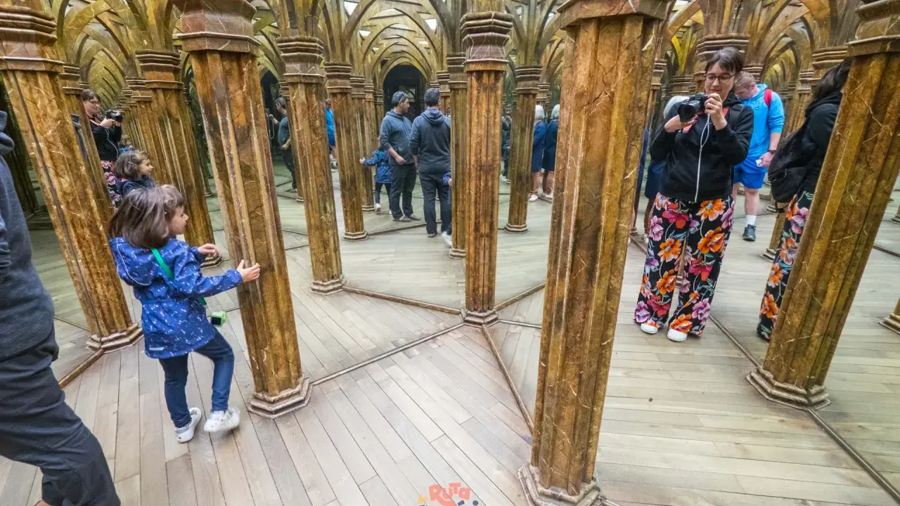 Niños exploran un laberinto de espejos con columnas doradas, creando un divertido juego de "praga con niños" y reflejos infinitos.