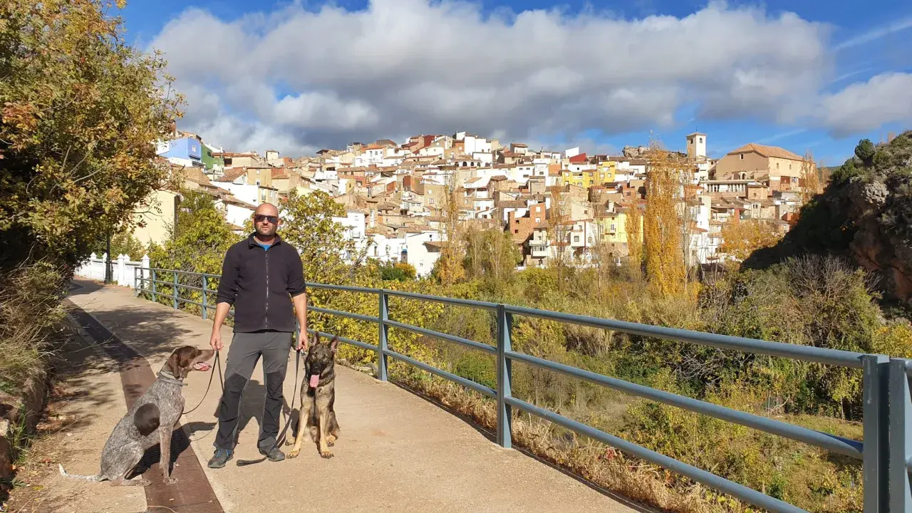 Hombre paseando con dos perros por la ruta de las esculturas de Bogarra, con el pueblo al fondo.