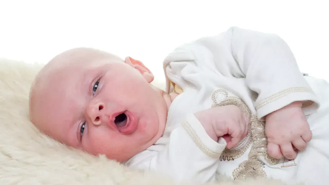 Baby mit offenem Mund, vielleicht husten. Was tun? Ein süßer kleiner Mensch auf weichem Fell.