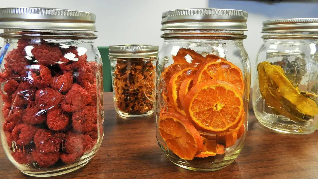 Vier Gläser mit getrockneten Früchten: Himbeeren, Orangenscheiben, etwas Braunes und etwas Gelbes. Perfekt zum glas beschriften für die Vorratshaltung.