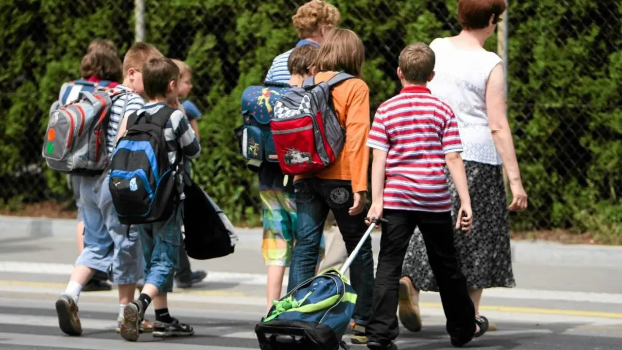 Niños con mochilas y un carrito cruzan la calle, marcando el regreso a la rutina de septiembre.
