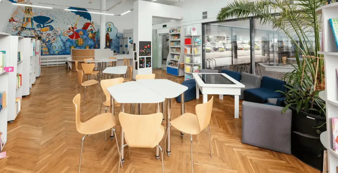 Spazi della scuola luminosi con scaffali, tavoli, sedie e un murale colorato. Un'area accogliente per imparare e giocare.
