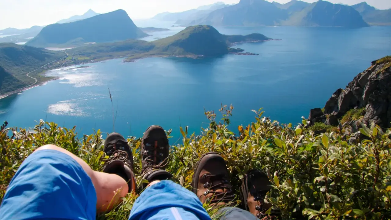 Vandringsskor vilar på en grön sluttning med en fantastisk utsikt över havet och bergen på Lofoten sommar.