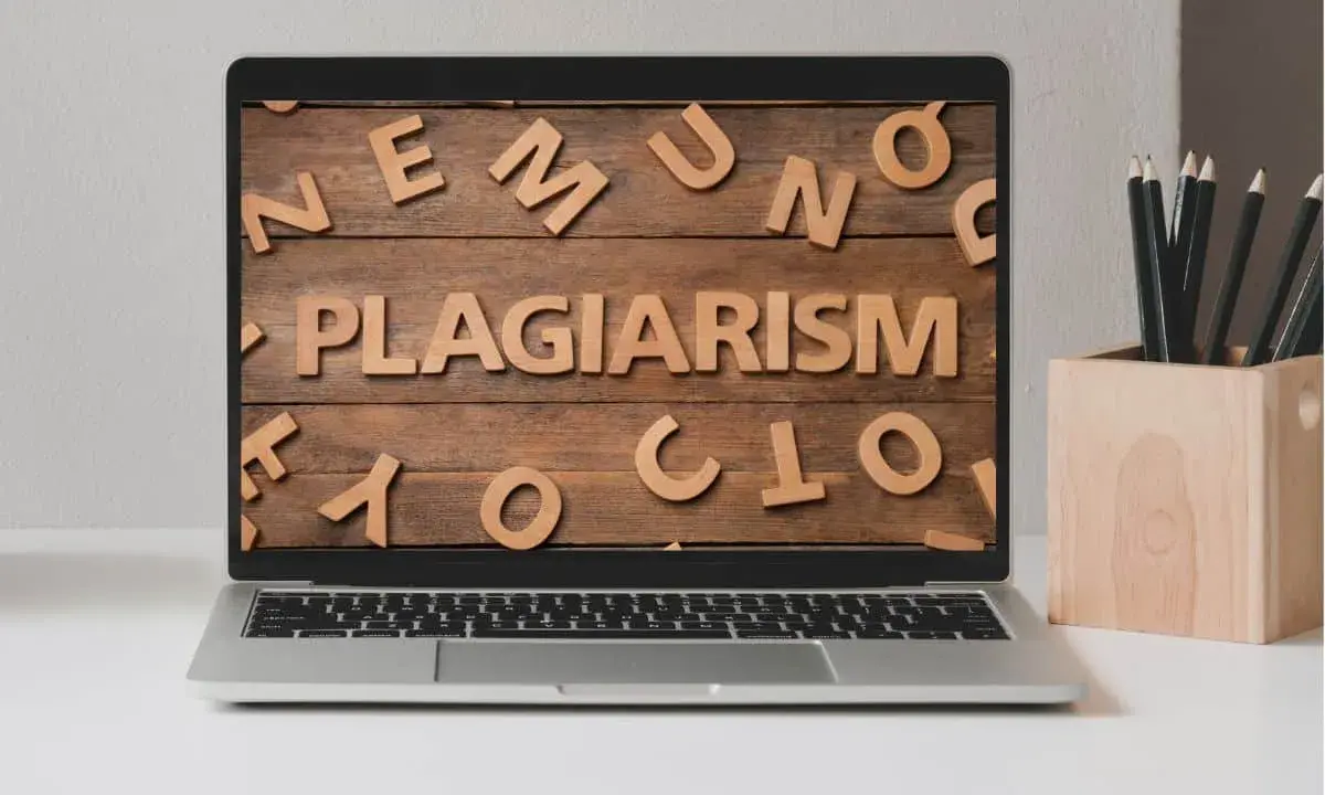 Laptop z napisem "PLAGIARISM" ułożonym z drewnianych liter na tle desek.