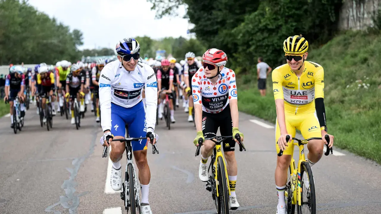 Radfahrer in bunten Trikots, Teil der Tour de France Teams, fahren auf der Straße. Einer trägt das Gelbe Trikot.
