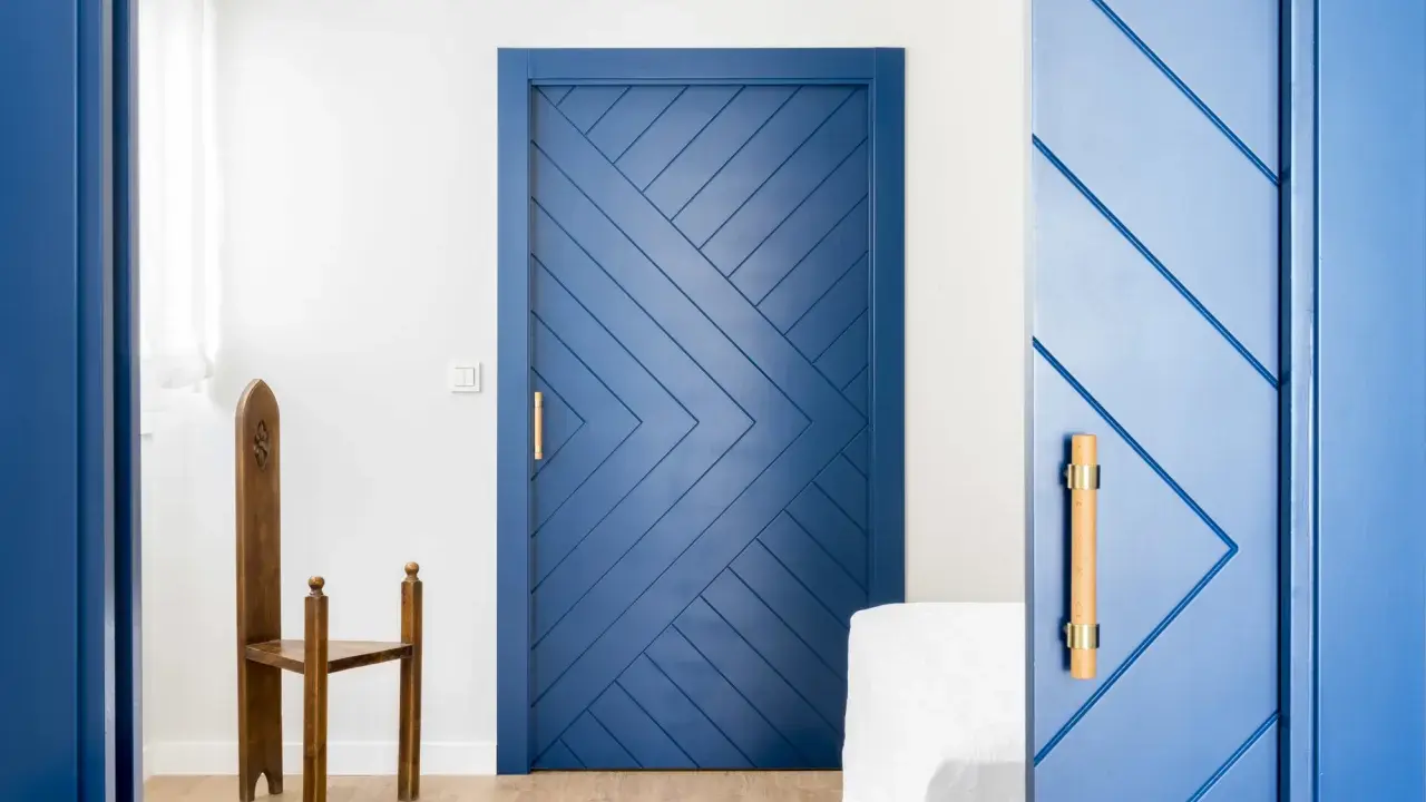 Puertas azules interiores con diseño geométrico y tiradores de madera. Una silla de madera antigua destaca junto a una de las puertas.