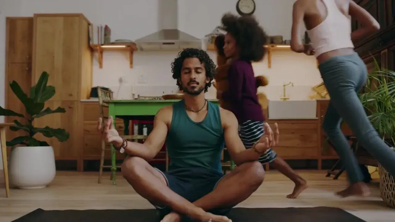 Man i lugn meditation i köket medan barn springer förbi. En lugn stund för 5 minute meditation mitt i vardagskaoset.