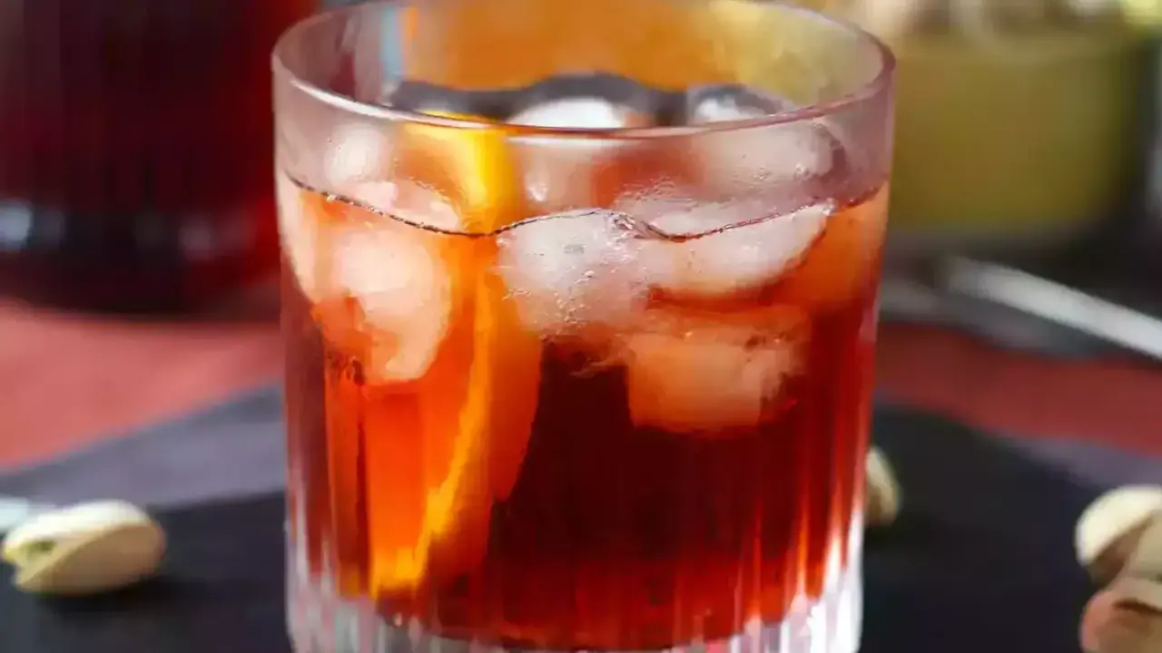 Orzeźwiający negroni sbagliato z lodem i plasterkiem pomarańczy, podany z pistacjami.