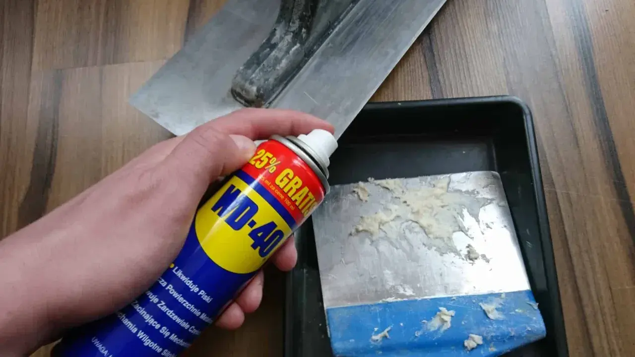 Spray WD-40 do czyszczenia zaschniętego betonu z narzędzi. Na zdjęciu puszka WD-40 i kielnia.