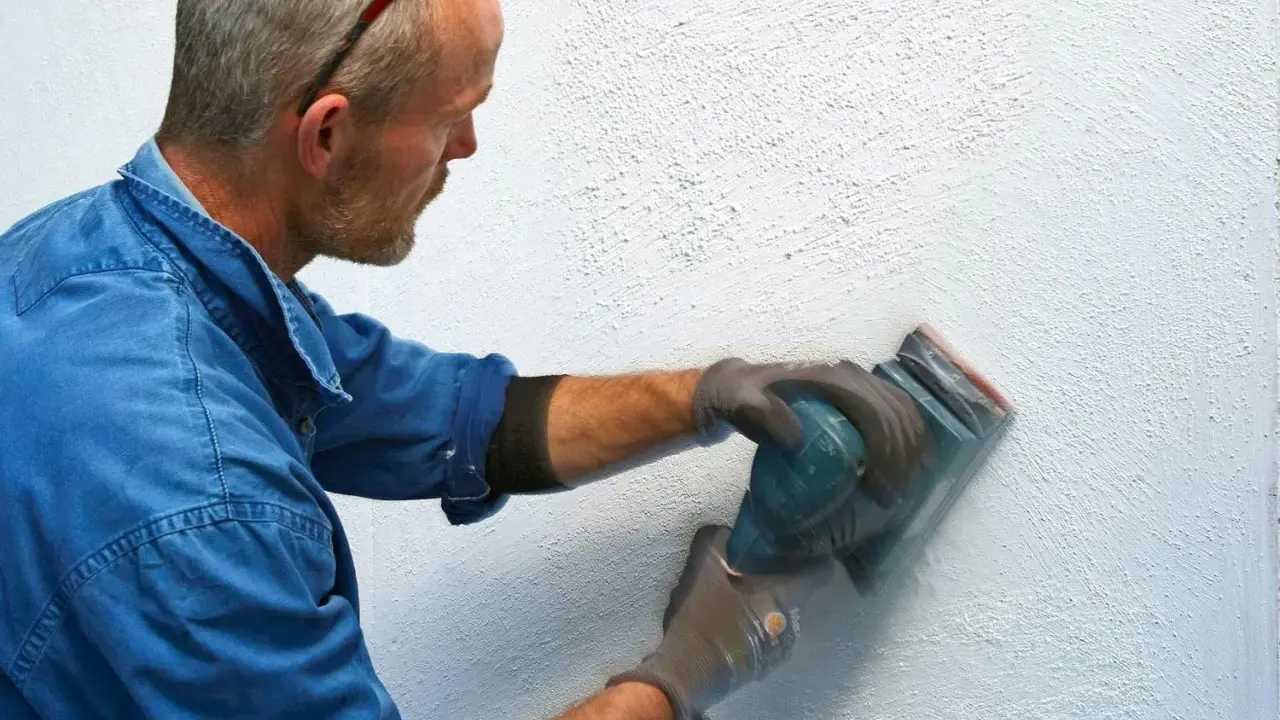 Man slipar en vägg med en excenterslip för att få bort slipdamm innan målning.