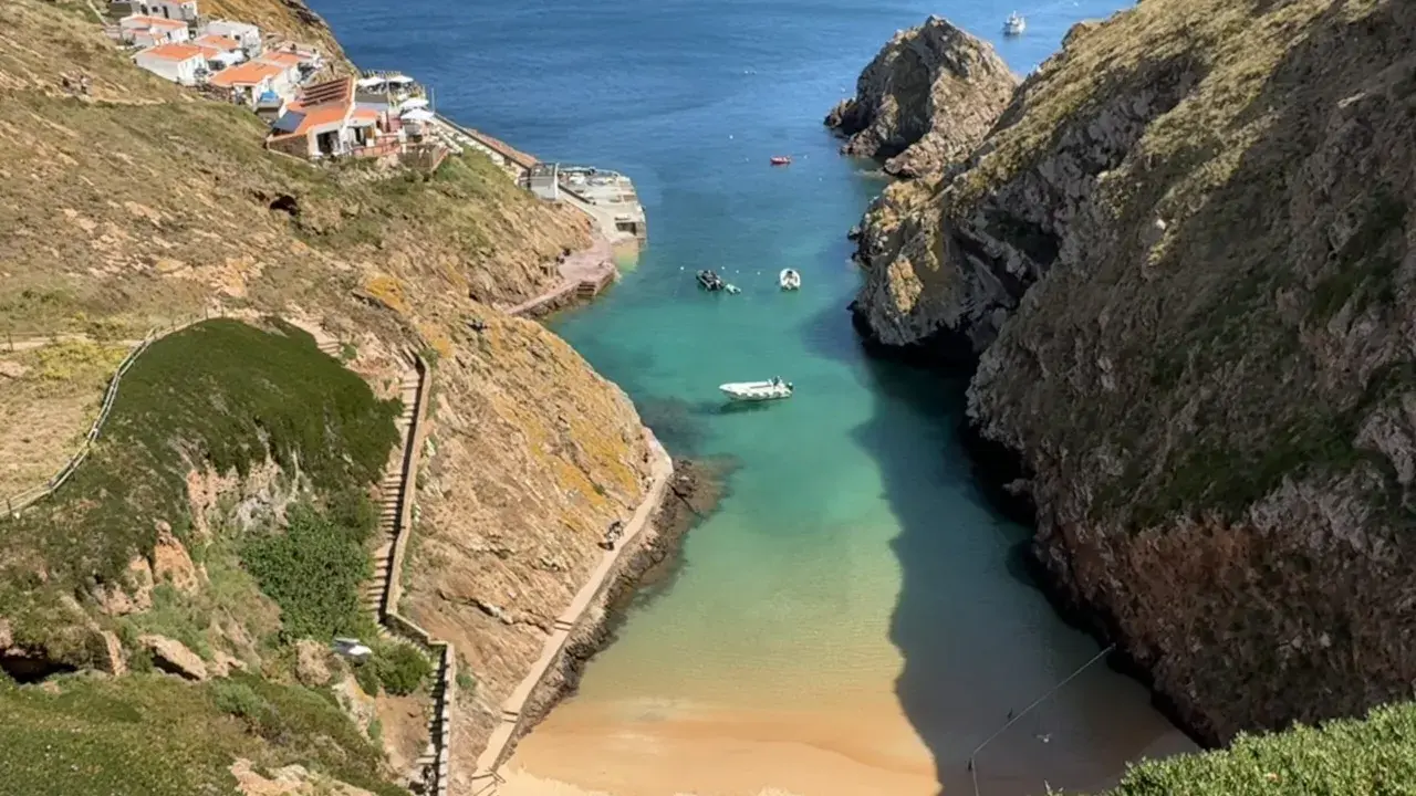 Idyllische Bucht mit weißem Sandstrand und türkisfarbenem Wasser auf den Berlengas Inseln. Kleine Boote ankern, Häuser schmiegen sich an die Felsen.