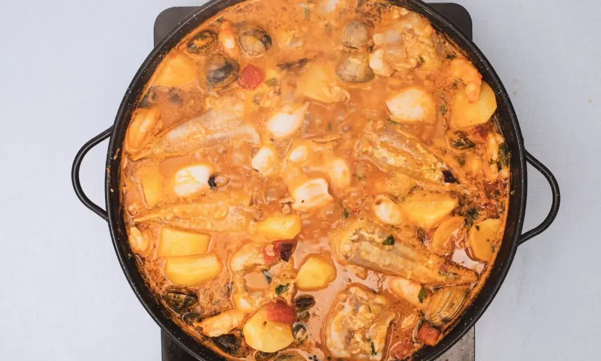 Un suquet de peix burbujeante en una paellera, con trozos de pescado, patatas, gambas y mejillones en una salsa naranja.