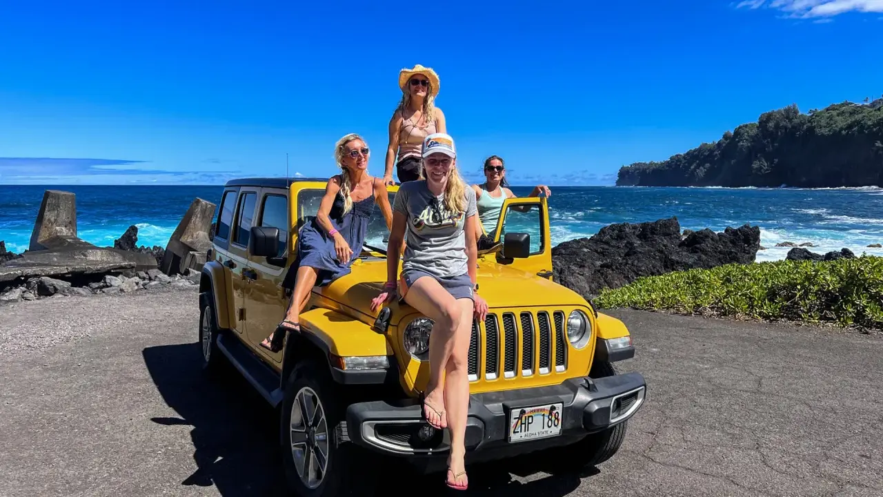 Fyra glada kvinnor på en gul jeep vid havet. Drömmen om att flytta till Hawaii känns nära!