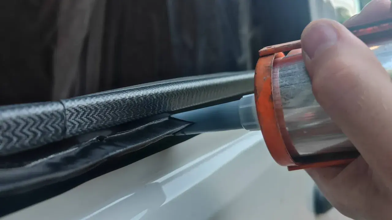 Application de mastic Sika 265 sur un joint de fenêtre de véhicule pour une étanchéité parfaite.