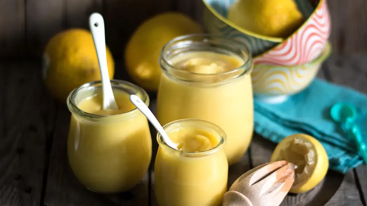 Drei Gläser mit cremigem Lemon Curd, Löffel und frische Zitronen. Perfekt für ein einfaches Lemon Curd Rezept.