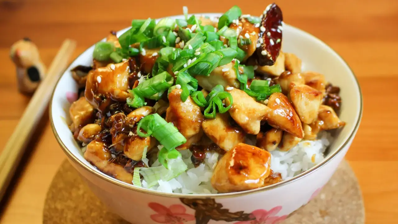Schüssel mit Reis, Hähnchen und Frühlingszwiebeln, garniert mit Sesam. Ein köstliches Kung Pao Gericht, bereit zum Genießen.