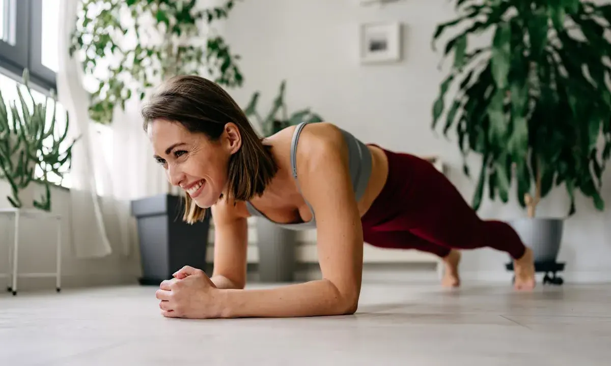Femme souriante en plein exercice de gainage, profitant d'un moment de bien-être à la maison.