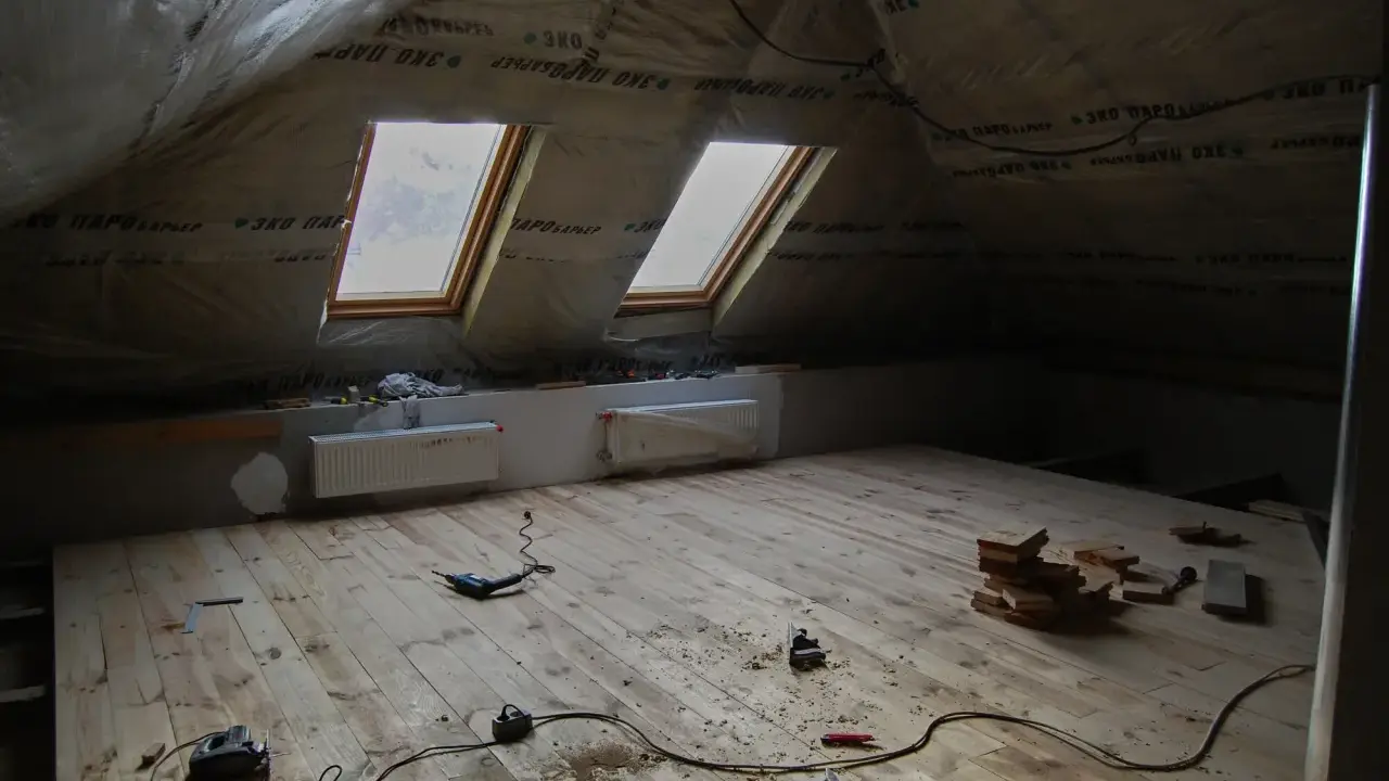 Chantier sous les combles : pose du frein vapeur, deux fenêtres de toit, radiateurs et outils sur le plancher en bois.