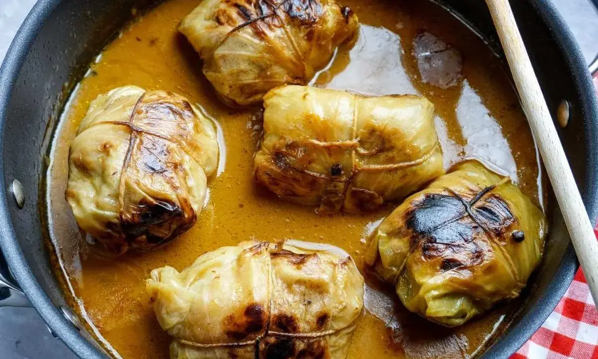 Fünf Kohlrouladen im Topf, bereit für ein köstliches Kohlrouladen Rezept. Eine Holzspatel liegt daneben.