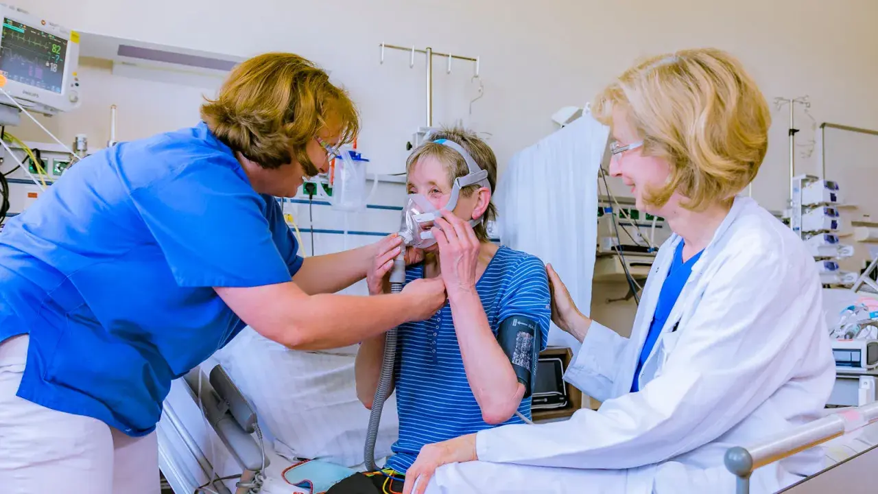 Ärztin und Pflegekraft helfen Patientin mit Lungenemphysem bei der Anpassung einer Beatmungsmaske. Medikamente sind Teil der Behandlung.