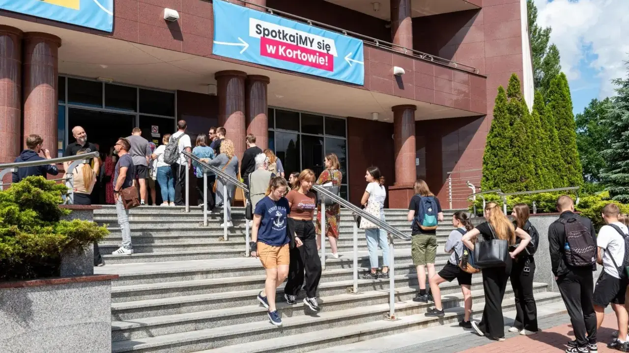 Grupa młodych ludzi schodzi po schodach przed budynkiem, gdzie wisi baner "Spotkajmy się w Kortowie!". To idealne miejsce na rozpoczęcie studiów w Olsztynie.