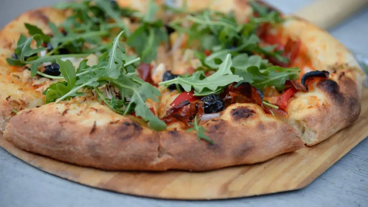 Pyszne ciasto na pizzę z rukolą, oliwkami i papryką, podane na drewnianej desce.