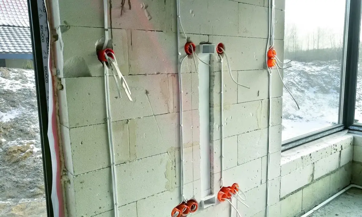 Instalacja elektryczna w ścianie z bloczków betonowych, etap prac wykończeniowych od stanu surowego zamkniętego. Widoczne puszki i przewody.