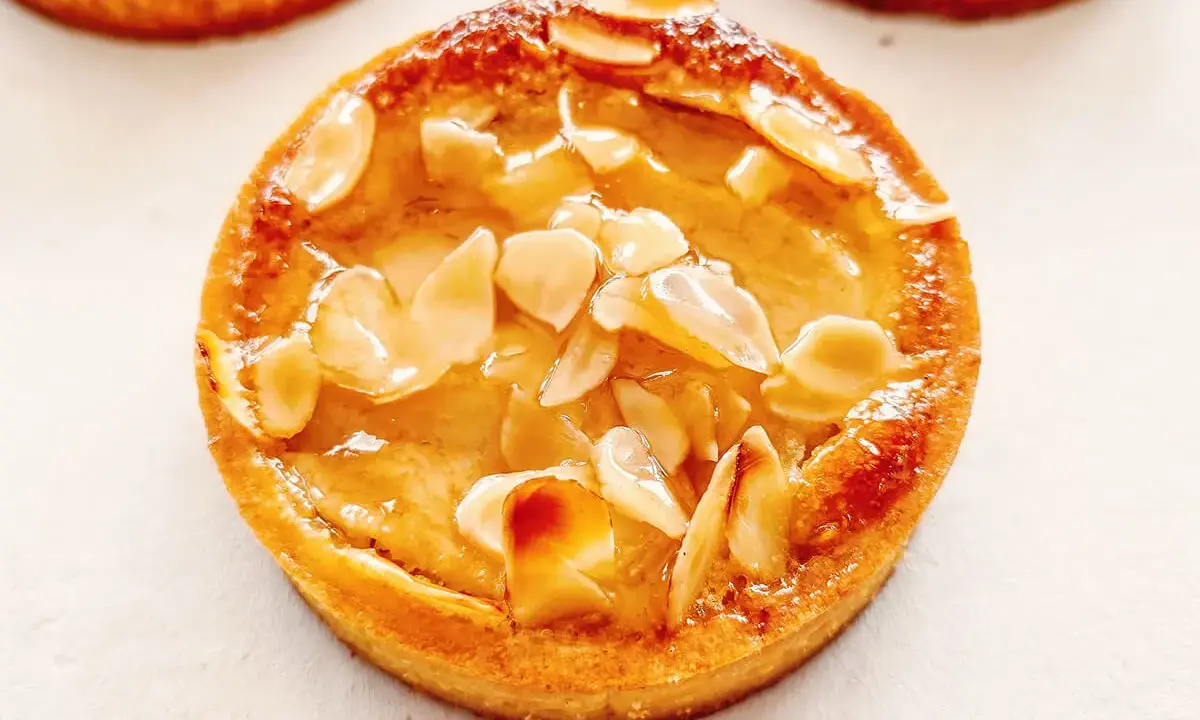 Un délicieux gâteau poire amandine, doré et garni d'amandes effilées, prêt à être dégusté.