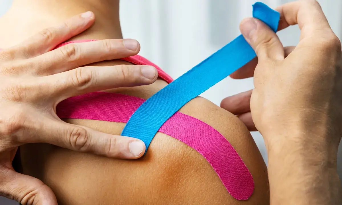 Aplikacja kinesiotapingu. Różowe i niebieskie plastry na ramieniu. Kinesiotaping co oznaczają kolory?