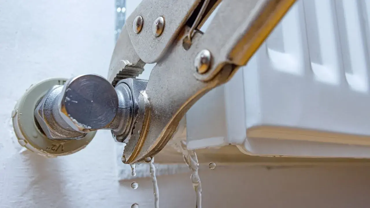 Pinzas sujetan una conexión de un radiador que gotea, con agua cayendo.
