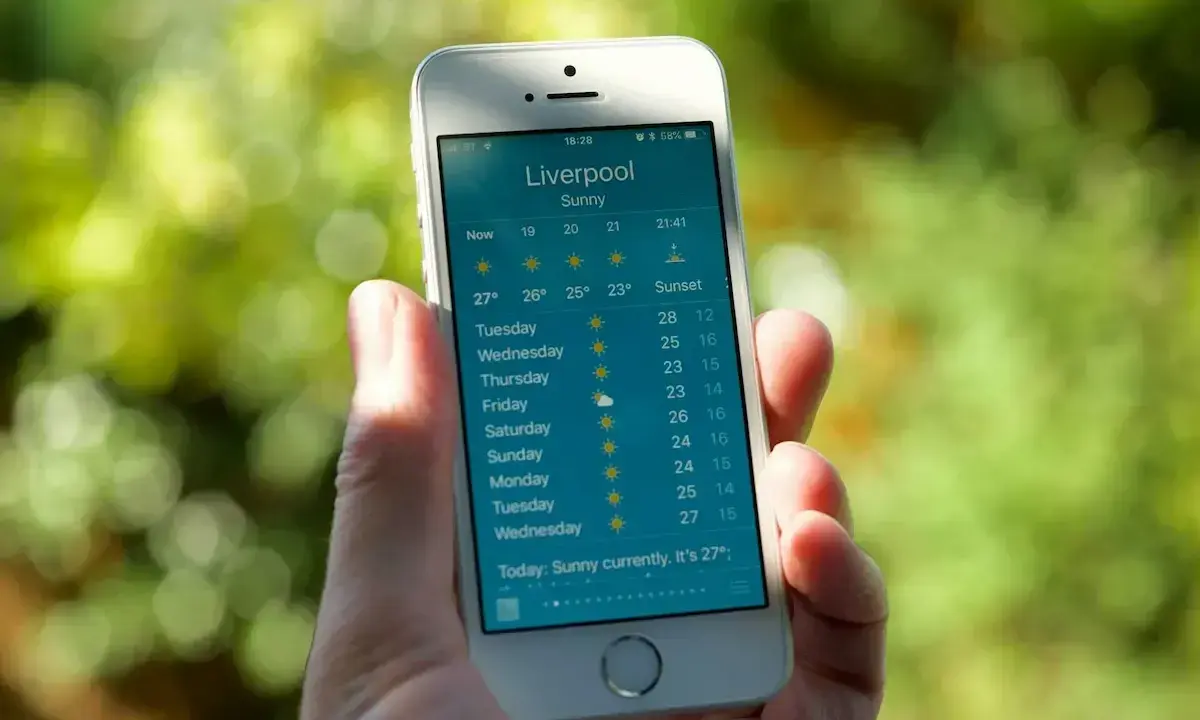 Dłoń trzyma smartfon z wyświetloną prognozą pogody dla Liverpoolu. To najlepsza aplikacja pogodowa, pokazująca słoneczną pogodę i temperatury na najbliższe dni.