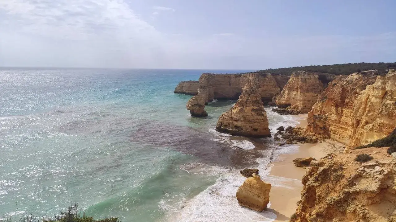 Acantilados dorados y mar turquesa en la ruta de los siete valles colgantes. Olas rompen en la arena de una playa escondida.