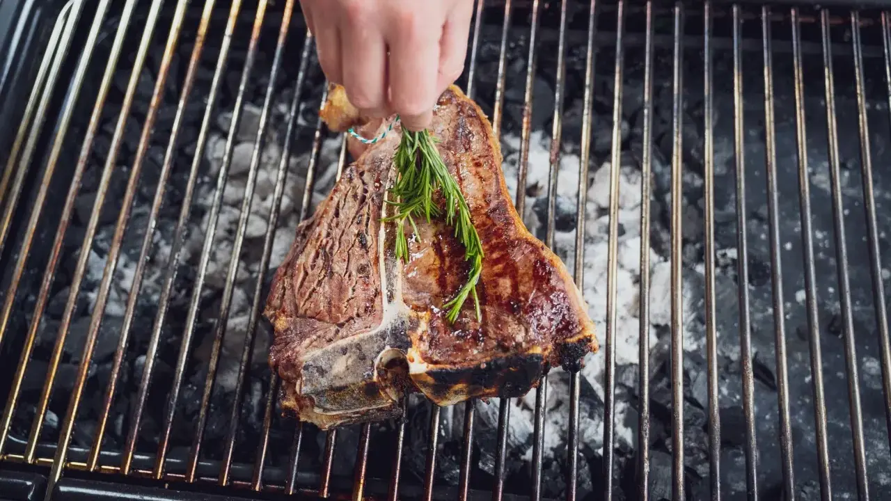 Ein saftiger florentiner steak wird mit Rosmarin auf dem Grill verfeinert.