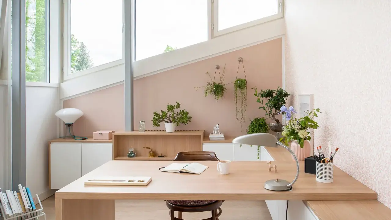 Une petite chambre avec bureau, lumineuse et décorée de plantes. Le bureau en bois clair est prêt pour le travail ou la lecture.