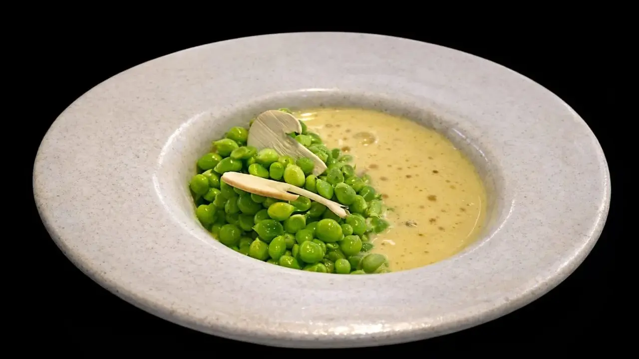 Un plato de guisantes de lágrima frescos con una cremosa sopa amarilla y una fina lámina de champiñón.