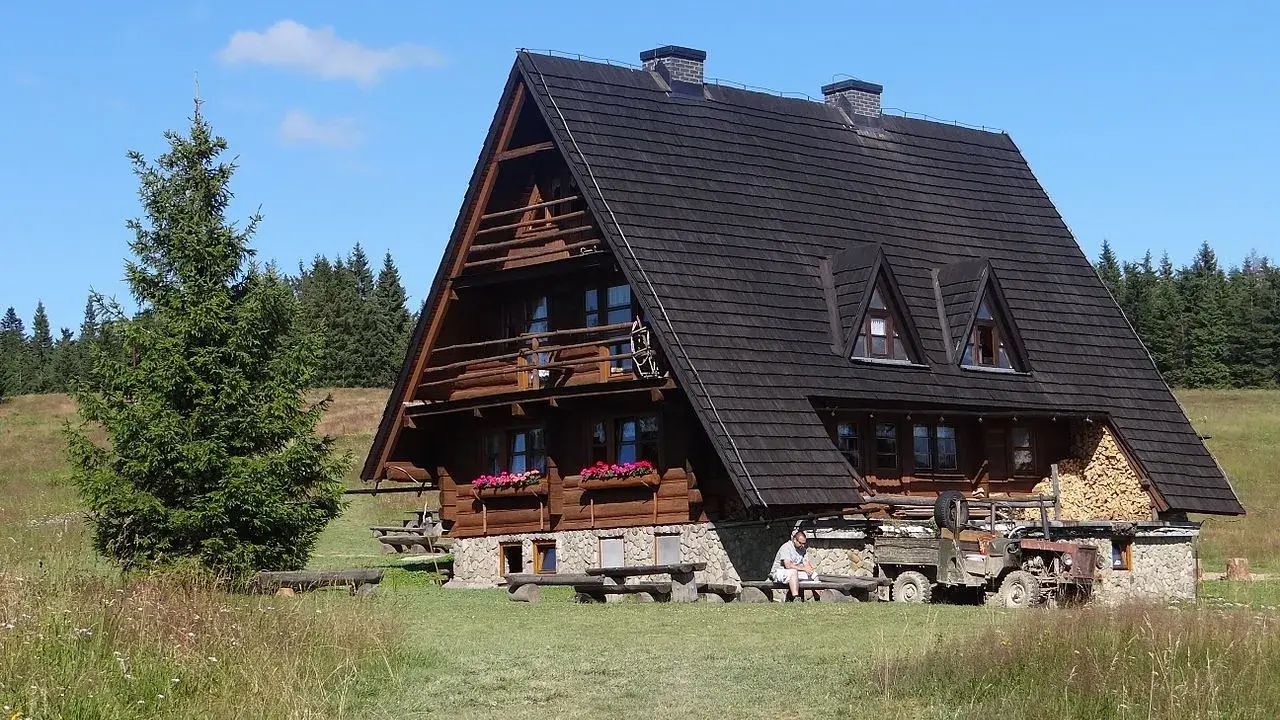 Drewniana bacówka na Krawcowym Wierchu, otoczona zielenią i lasem. Obok stoi stary traktor.