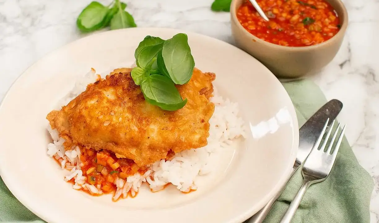 Krispig kyckling piccata serverad på ris med en smakrik tomatsås och färsk basilika. En härlig måltid!